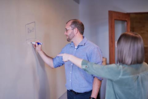 Joe draws site map on whiteboard while coworker points at it