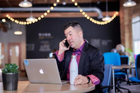 Brett converses with client over the phone while sitting in front of his laptop