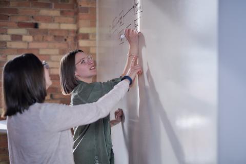 Haley outlines user workflow on whiteboard while coworker points to part of it