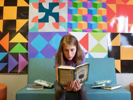 Student sits on bench reading a book in front of artwork